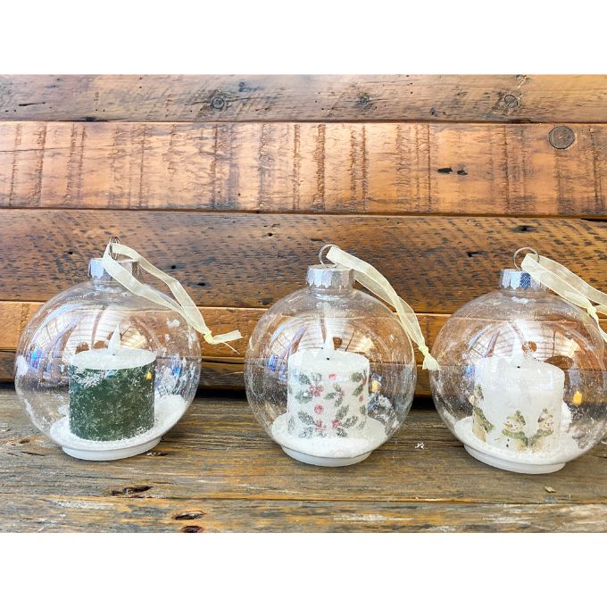 Three clear glass ball ornaments with candles inside on a wooden surface. Ball Ornaments with LED Candles - Three Styles available at Quilted Cabin Home Decor.