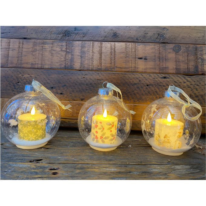 Three glass ornaments with lit candles inside on a wooden surface. Ball Ornaments with LED Candles - Three Styles available at Quilted Cabin Home Decor.