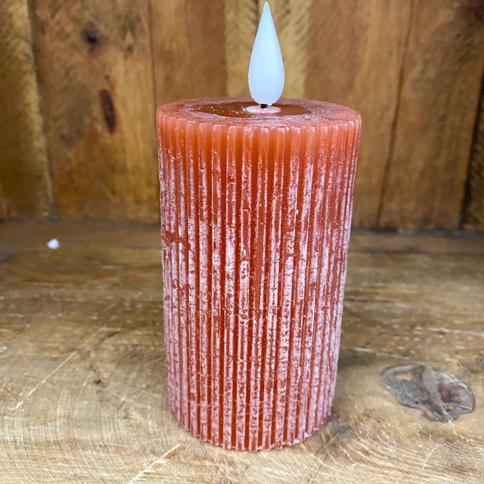 Textured orange candle with a white wick on a wooden surface. Orange Ridged LED 4" Votive Candle available at Quilted Cabin Home Decor.