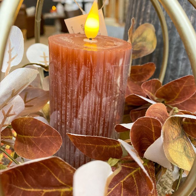 Decorative orange candle with leaves and a blurred background. Orange Ridged LED 4" Votive Candle available at Quilted Cabin Home Decor.