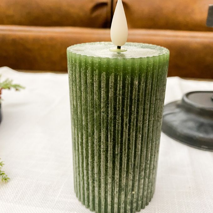 Green textured candle with a white wick on a white surface. Green Ridged LED 4" Votive Candle available at Quilted Cabin Home Decor.