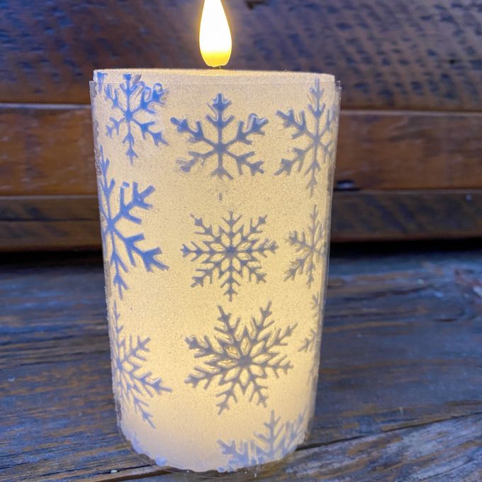 Candle with snowflake pattern on a wooden surface.  White Snowflake LED 5" Pillar Candle available at Quilted Cabin Home Decor.
