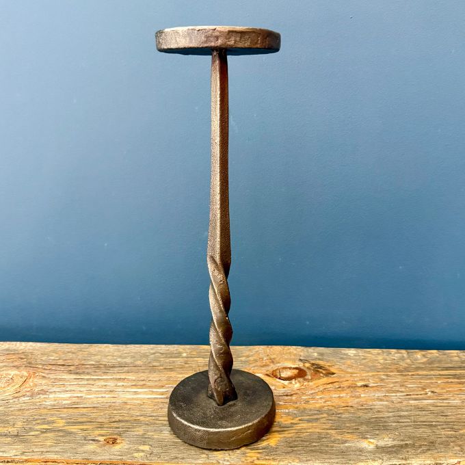 A rustic blackened metal stand shaped like a twisted drill bit with a circular top and base candle holder.  Comes in two sizes available at Quilted Cabin in Airdrie