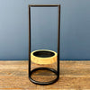 A modern floating candle holder featuring a black metal frame and a light natural wood ring floating inside a clear glass container, set on a rustic wooden table against a slate blue background.  Candle holder available at Quilted Cabin in Airdrie
