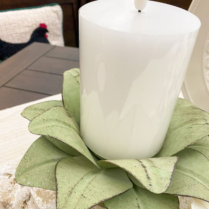 White candle on a green metal leafy holder. Green Floral Tin Candle Holder available at Quilted Cabin Home Decor.