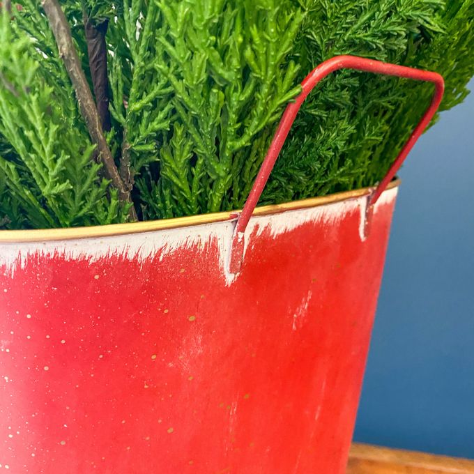 Red & White Tree Wall Bucket is a tall red metal bucket with white christmas trees and snowflakes along the bottom of it. Available at Quilted Cabin Home Decor.