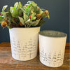 White Distressed Galvanized Tree Buckets - Two Sizes are shown. Two white metal buckets with embossed trees on the outside to fill with holiday florals. Available at Quilted Cabin Home Decor.