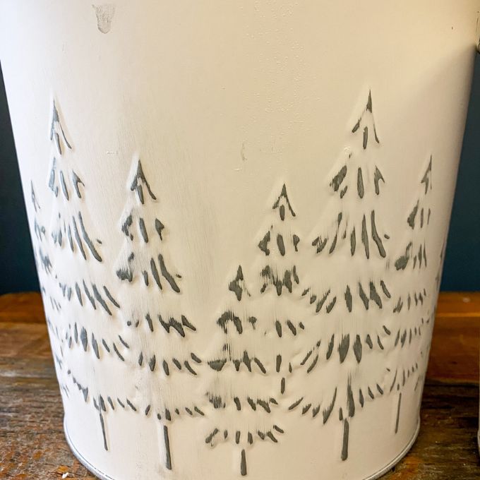 White Distressed Galvanized Tree Buckets - Two Sizes are shown. Two white metal buckets with embossed trees on the outside to fill with holiday florals. Available at Quilted Cabin Home Decor.