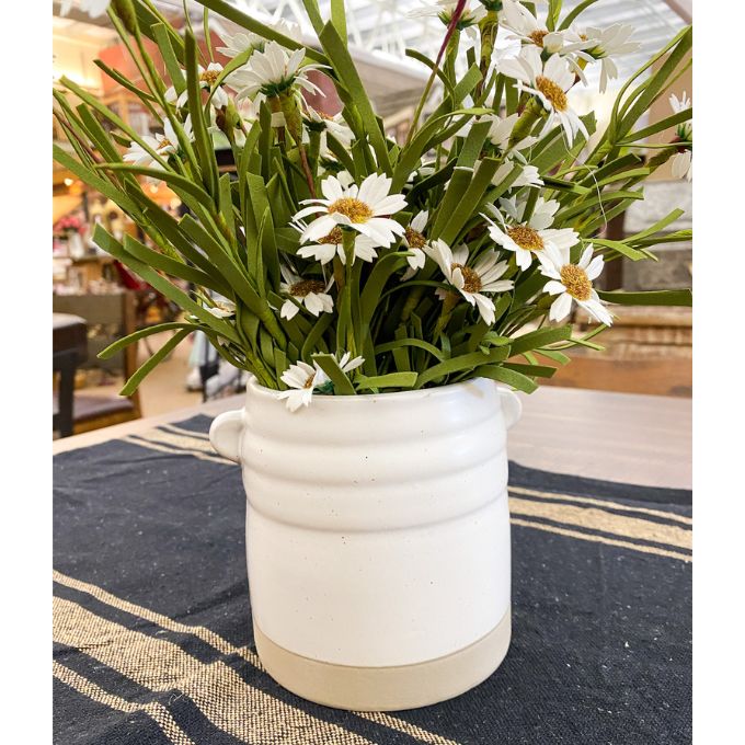 White ceramic planter with green plants and white flowers on a striped tablecloth. White Farmhouse-Styled Ceramic Jar available at Quilted Cabin Home Decor.