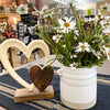 Heart-shaped wooden ornament and white flower pot on a table with a store interior background. White Farmhouse-Styled Ceramic Jar available at Quilted Cabin Home Decor.