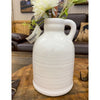 White ceramic vase with a handle on a wooden table, featuring a flower arrangement. White Porcelain Jug-Style Vase available at Quilted Cabin Home Decor. 