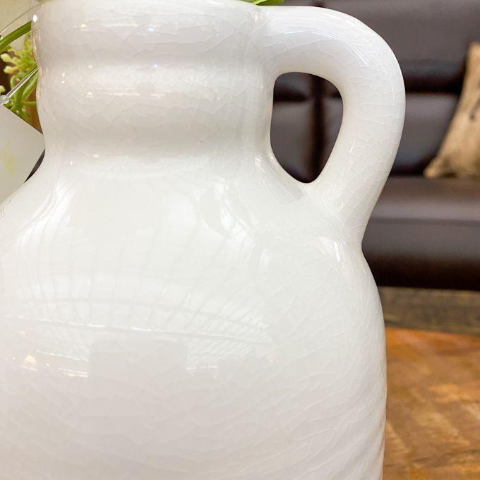 White ceramic pitcher on a wooden surface with a blurred background. White Porcelain Jug-Style Vase available at Quilted Cabin Home Decor. 