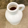 White ceramic pitcher against a stone wall background. White Porcelain Jug-Style Vase available at Quilted Cabin Home Decor. 