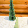 Green paper Christmas tree on a textured surface with wooden background. Vintage Green Paper Trees - Two Sizes available at Quilted Cabin Home Decor.