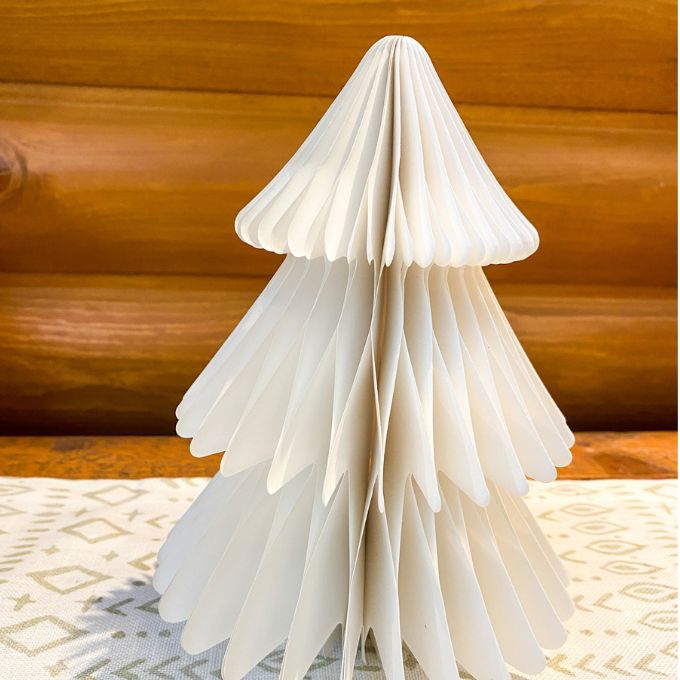 White paper Christmas tree on a wooden surface with a patterned rug underneath. Vintage White Paper Trees - Three Sizes available at Quilted Cabin Home Decor.
