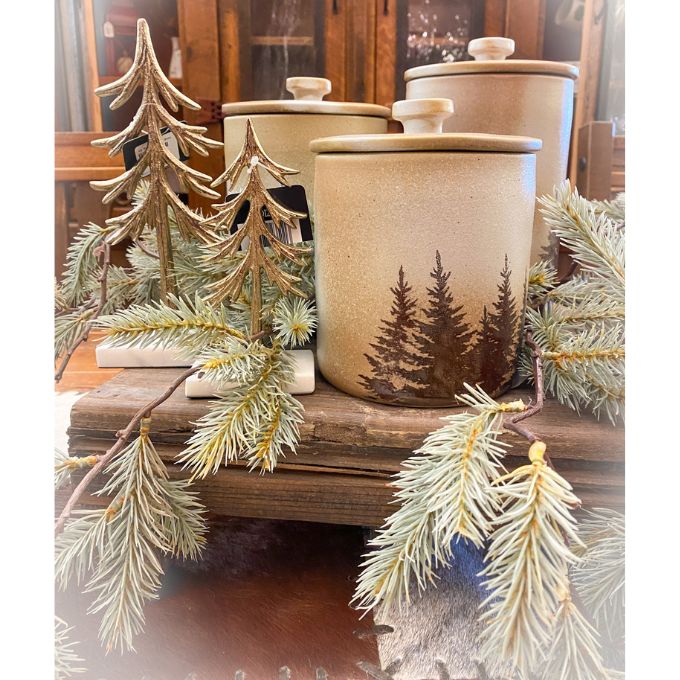 Two Gold trees on a white marble look base along with christmas greens and kitchen canisters.