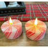 Two striped candles with flames on a wooden surface with a red checkered cloth in the background. Short Peppermint Votive LED Timer Candles - Set of Two available at Quilted Cabin Home Decor.