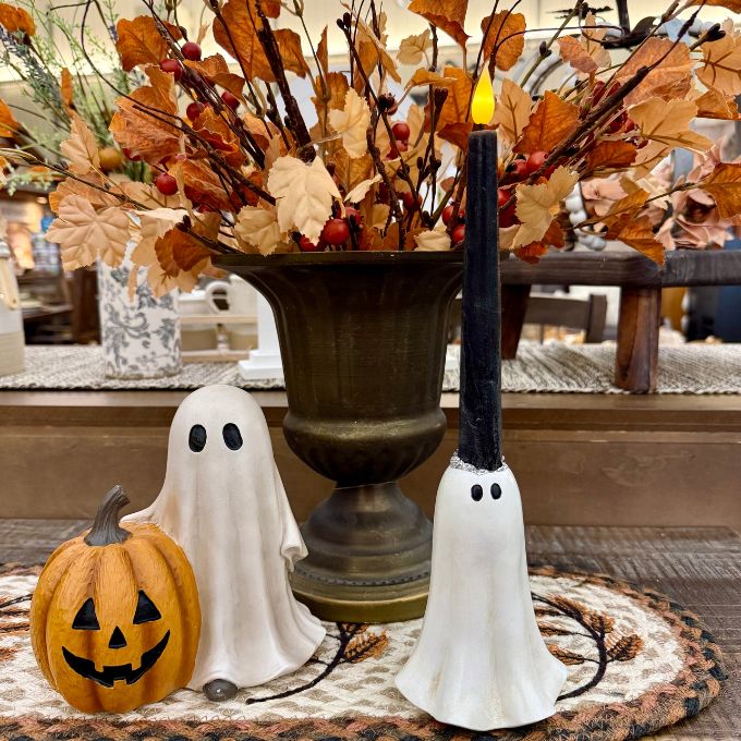 Halloween-themed tabletop decor set featuring a carved orange jack-o'-lantern, a white ghost figurine, a black pillar candle with a white ghost base, and a large bronze urn filled with autumn leaves and berries. Available at Quilted Cabin in Airdrie