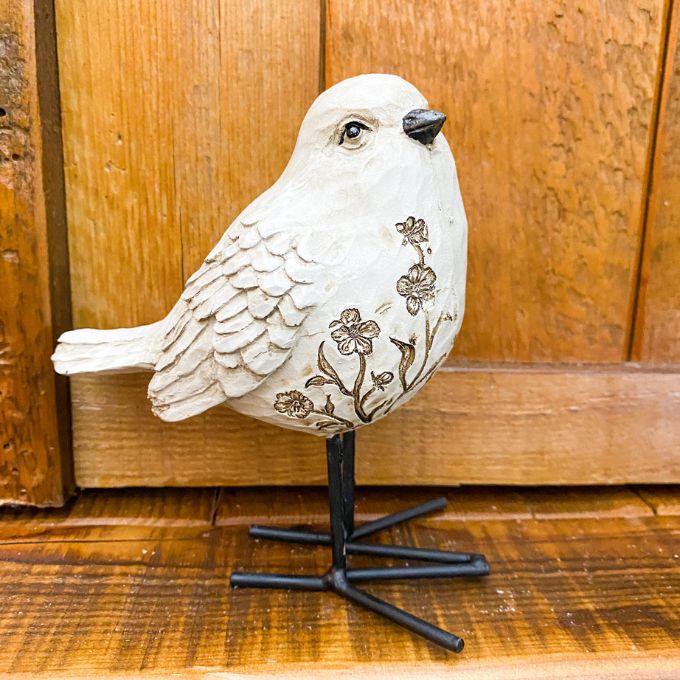 Decorative white bird figurine with floral patterns against a wooden background. Engraved Floral Bird Figurine available at Quilted Cabin Home Decor.