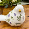 Ceramic bird figurine with floral patterns on a wooden surface. Painted Floral Porcelain Bird available at Quilted Cabin Home Decor.