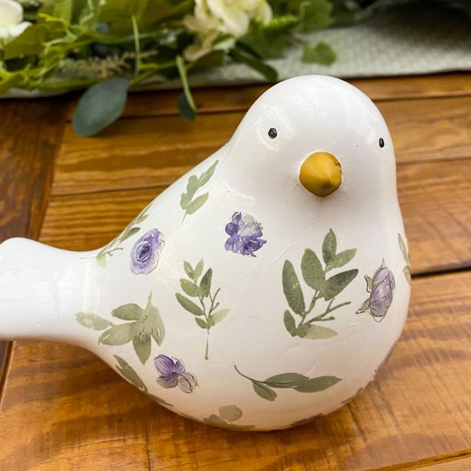 Ceramic bird figurine with floral patterns on a wooden surface. Painted Floral Porcelain Bird available at Quilted Cabin Home Decor.