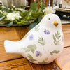 Ceramic bird figurine with floral patterns on a wooden surface. Painted Floral Porcelain Bird available at Quilted Cabin Home Decor.