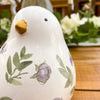 Decorative ceramic bird with floral designs on a wooden surface. Painted Floral Porcelain Bird available at Quilted Cabin Home Decor.