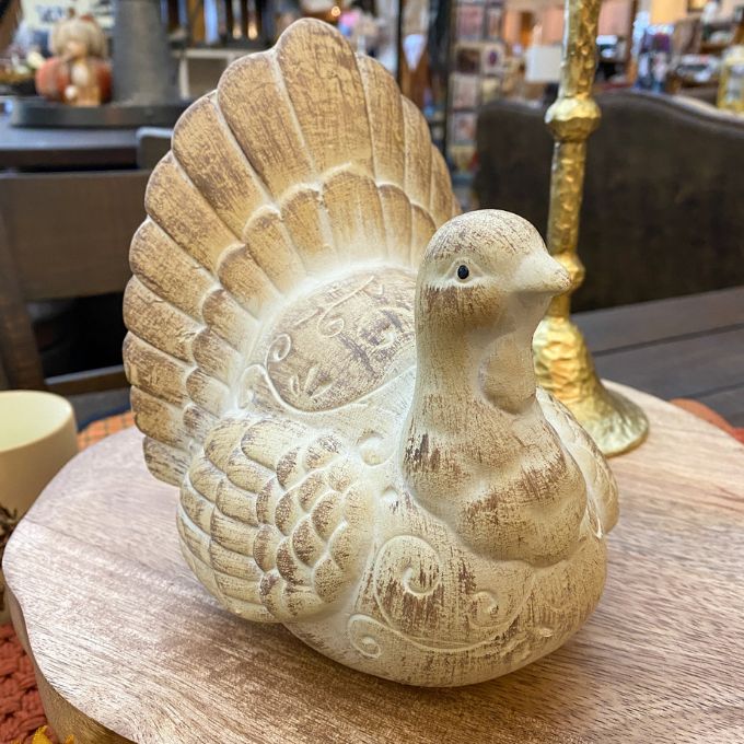 Decorative wooden turkey sculpture on a wooden surface with a blurred background. Weathered Resin Turkey available at Quilted Cabin Home Decor.