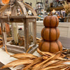 A Three Stack pumpkin in a deep orange color is shown with other fall decor items. Available at Quilted Cabin Home Decor.