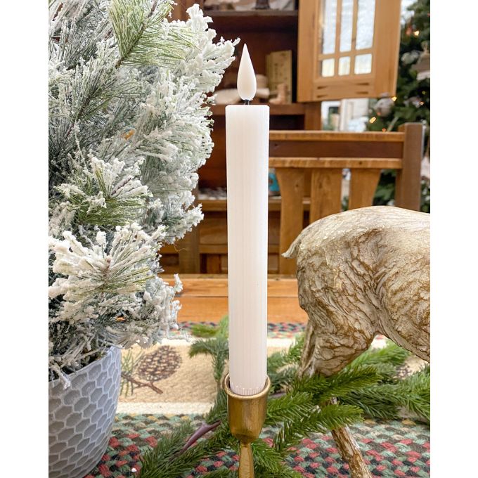 Tall white candle in a gold holder on a Christmas tree with a wooden cabinet in the background. White Ridged LED Timer Taper Candles - Two Sizes available at Quilted Cabin Home Decor.