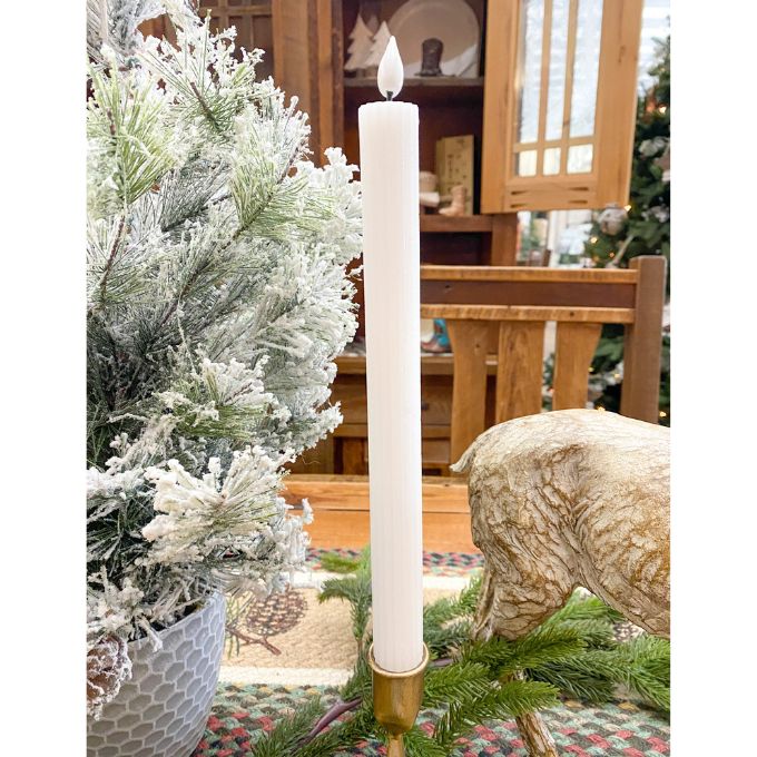 Tall white candle in a wooden holder on a table with a Christmas tree and decorative items in the background. White Ridged LED Timer Taper Candles - Two Sizes available at Quilted Cabin Home Decor.