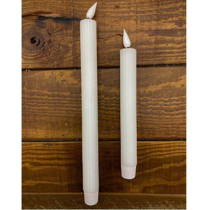Two white candles with flame tips on a wooden surface. White Ridged LED Timer Taper Candles - Two Sizes available at Quilted Cabin Home Decor.