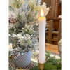 Decorative candle in a gold holder with a Christmas tree in the background. White Ridged LED Timer Taper Candles - Two Sizes available at Quilted Cabin Home Decor.