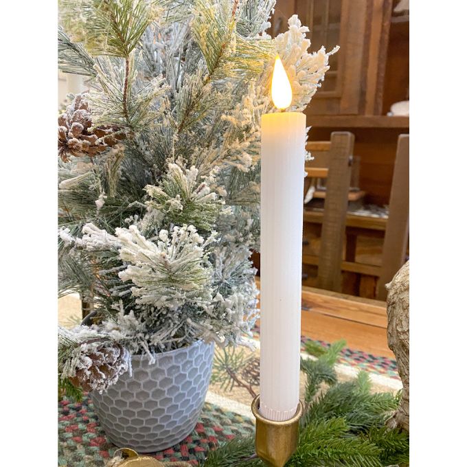 Decorative candle in a gold holder with a Christmas tree in the background. White Ridged LED Timer Taper Candles - Two Sizes available at Quilted Cabin Home Decor.