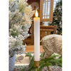 Decorative candle in a gold holder with Christmas trees and a wooden bench in the background. White Ridged LED Timer Taper Candles - Two Sizes available at Quilted Cabin Home Decor.