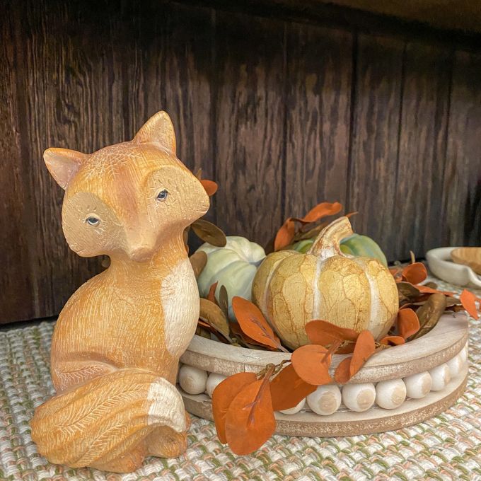 A tan fox figurine with a white chest and white tipped tail sits beside a pumpkin display. Available at Quilted Cabin Home Decor.