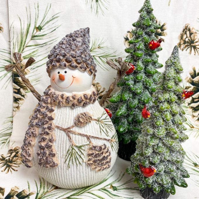 A smiley acorn topped snowman with an acorn scarf and twig style arms is shown with two resin evergreen trees. Available from Quilted Cabin Home Decor.