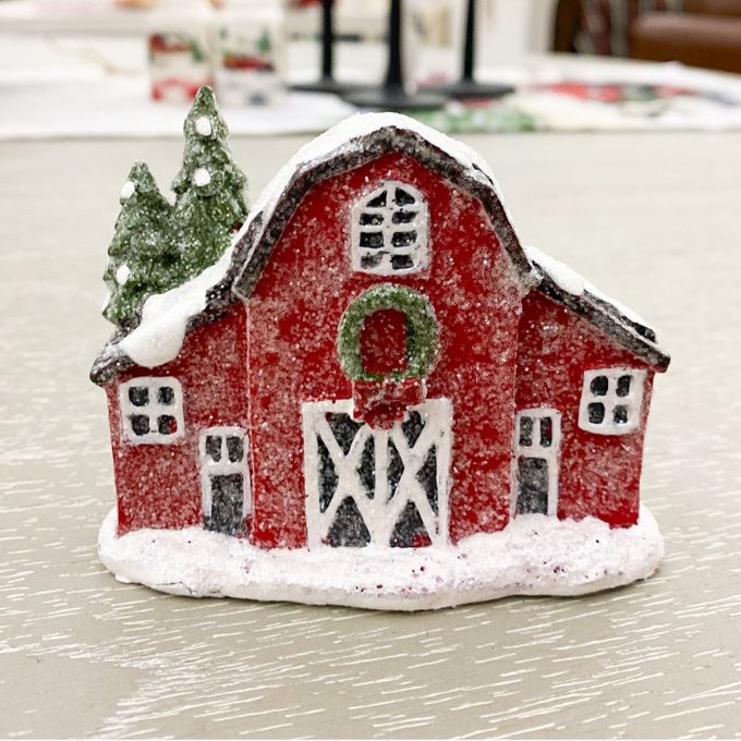 Small red barn figurine with snow on a light background. Snowy Red Barn Figurine available at Quilted Cabin Home Decor.