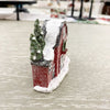 Small decorative barn with snow on a light gray surface. Snowy Red Barn Figurine available at Quilted Cabin Home Decor.
