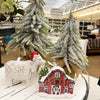 Decorative Christmas scene with a cow figurine, small red barn, and trees in a store setting. Snowy Red Barn Figurine available at Quilted Cabin Home Decor.