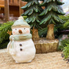 Decorative snowman figurine with a green hat and scarf in front of a Christmas tree. Green Hat Snowman Figurine available at Quilted Cabin Home Decor.