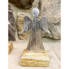 Metal angel sculpture on a wooden base against a stone wall background. Midnight Shimmer Angels - Two Sizes available at Quilted Cabin Home Decor.