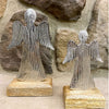 Two angel figurines made of metal on wooden bases against a stone wall background. Midnight Shimmer Angels - Two Sizes available at Quilted Cabin Home Decor.