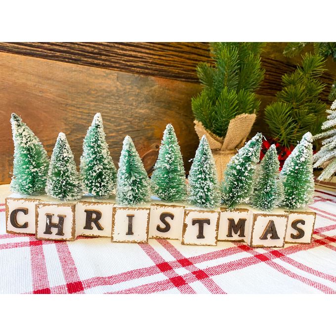 Winter Sparkle Forest Christmas Block Shelf Sitter is a group of blocks with black letters to spell the word Christmas and each black has a green bottle brush tree on it. Available at Quilted Cabin Home Decor.