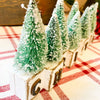 Winter Sparkle Forest Christmas Block Shelf Sitter is a group of blocks with black letters to spell the word Christmas and each black has a green bottle brush tree on it. Available at Quilted Cabin Home Decor.