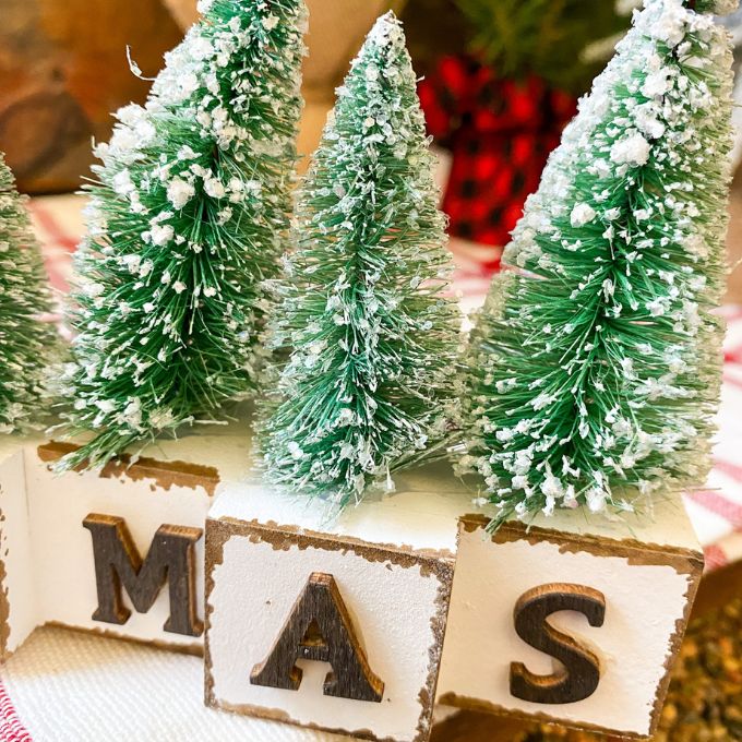 Winter Sparkle Forest Christmas Block Shelf Sitter is a group of blocks with black letters to spell the word Christmas and each black has a green bottle brush tree on it. Available at Quilted Cabin Home Decor.