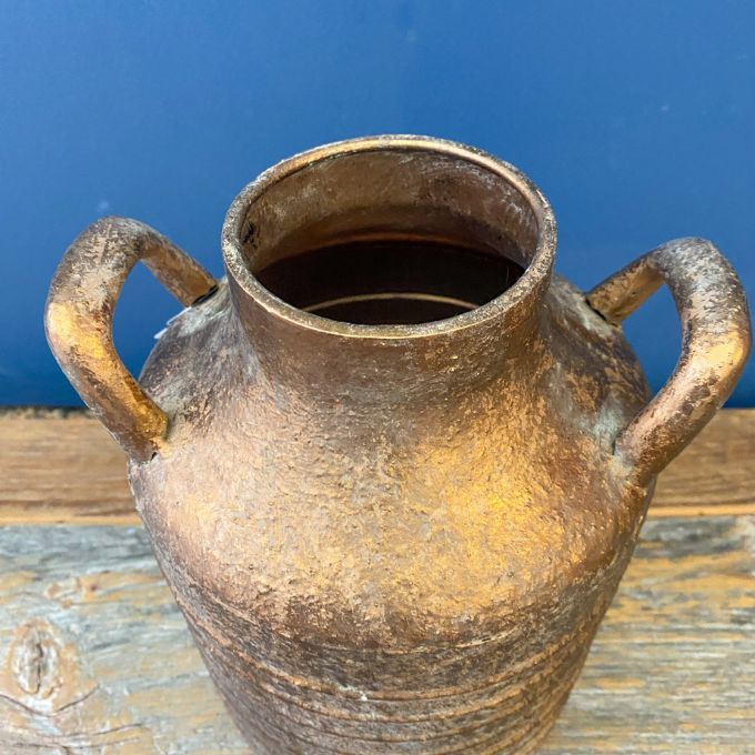 Rustic gold vase with handles on a wooden surface against a blue background. Gold Metal Milk Can Vase available at Quilted Cabin Home Decor.