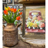 Decorative vase with orange tulips next to a framed picture of a truck with flowers on a wooden surface. Gold Metal Milk Can Vase available at Quilted Cabin Home Decor.
