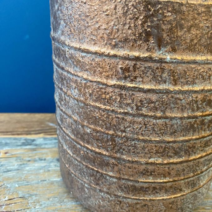 Rustic metal container with concentric circular patterns on a wooden surface. Gold Metal Milk Can Vase available at Quilted Cabin Home Decor.