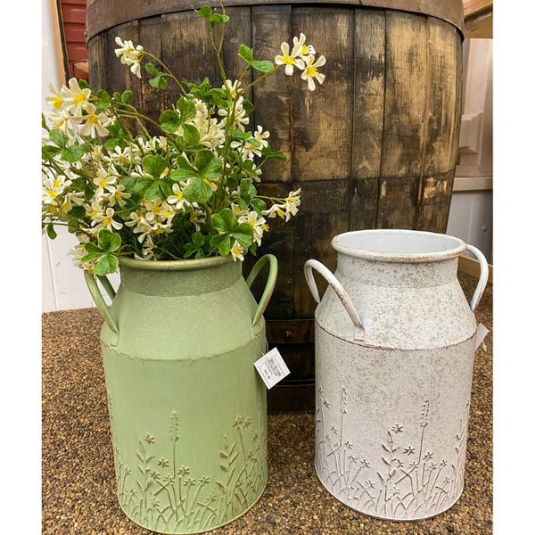 Two metal jugs, one green and one white, with floral decorations, next to a wooden barrel. Embossed Metal Milk Cans - Two Colours available at Quilted Cabin Home Decor.